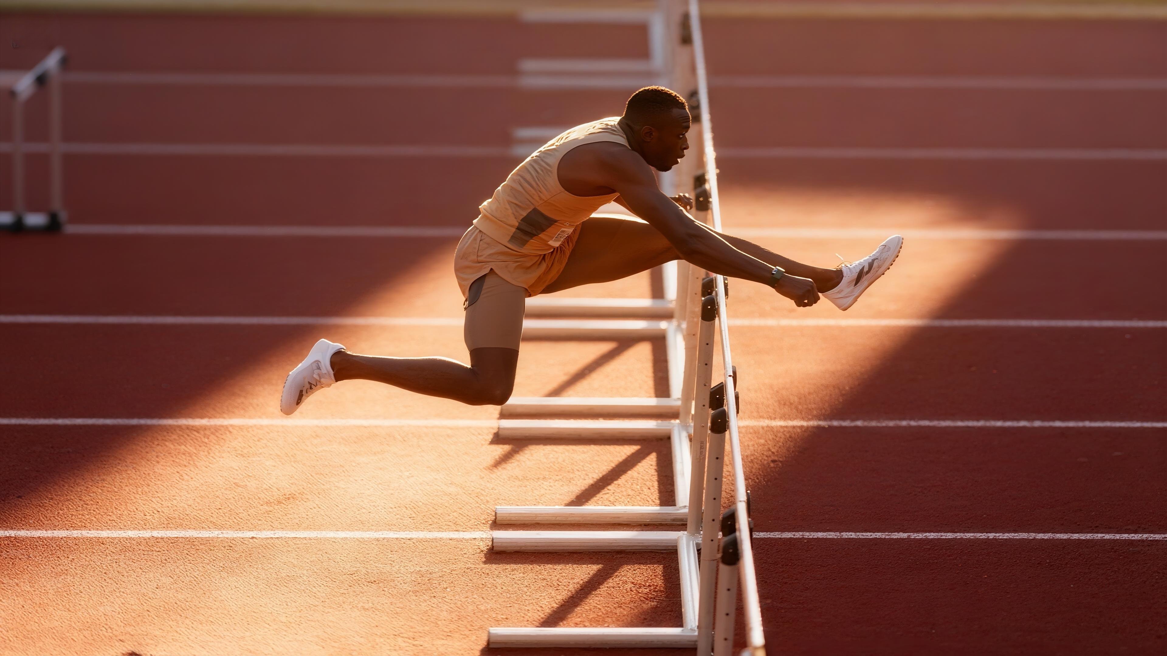 Atleta saltando vallas en pista de atletismo al atardecer - Impulsa tu carrera deportiva