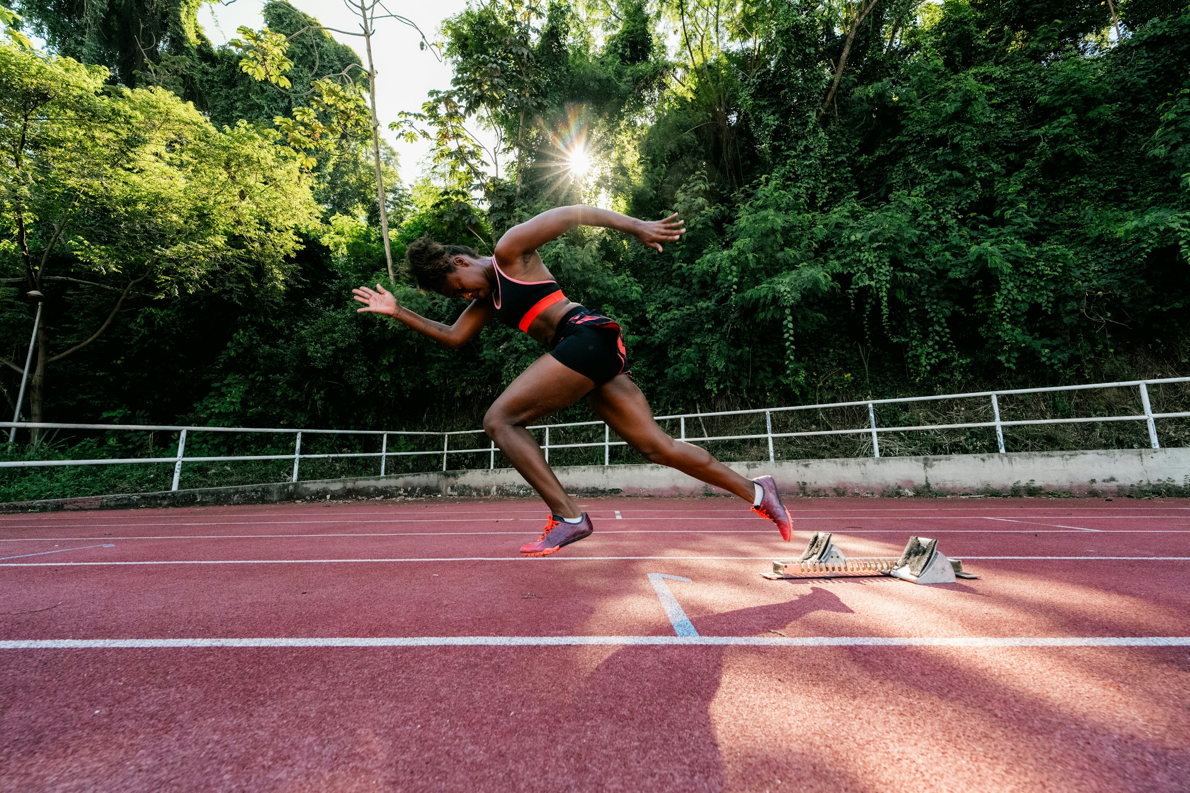 Atleta femenina arrancando desde los bloques de salida en pista de atletismo - Impulsa tu carrera deportiva